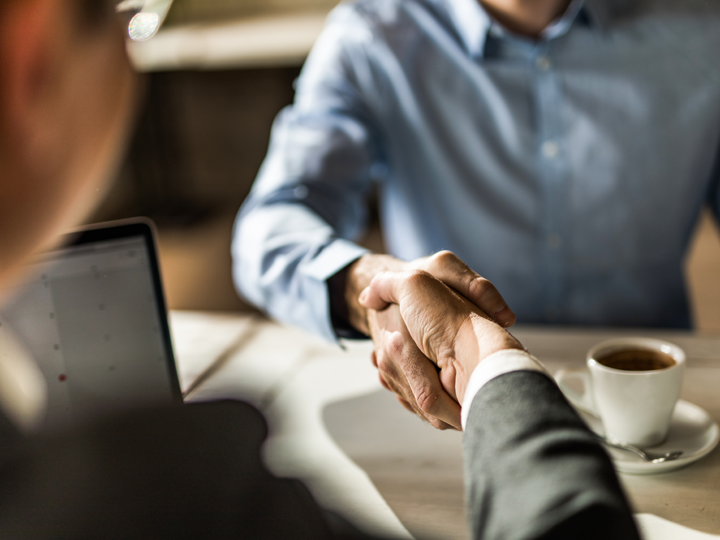 Two male colleagues shaking hands sitting down at office desk