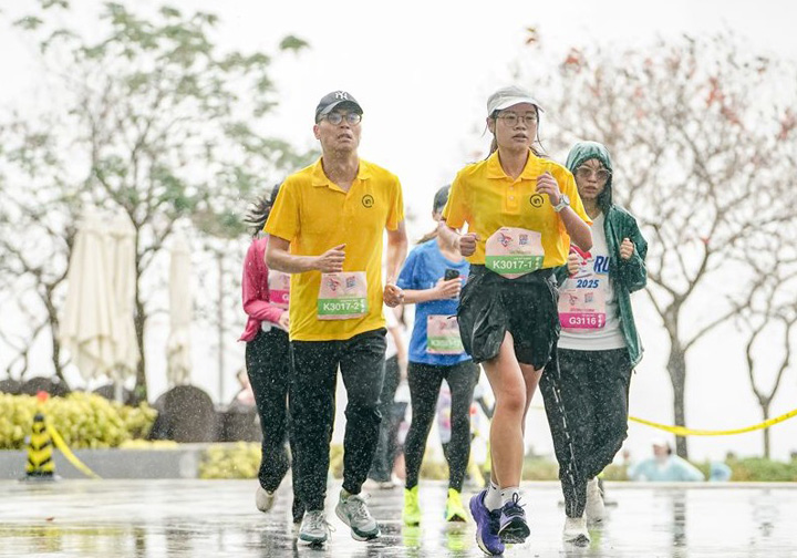 A man and a woman run in the rain wearing yellow Intertek t-shirts.