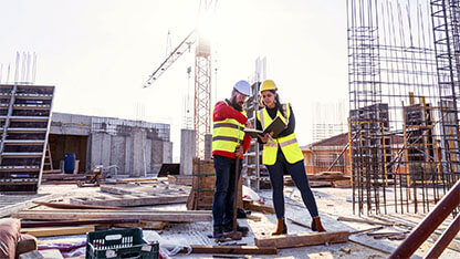 A Teamwork of an Architect - Project Manager and a Construction worker at site of a reinforced concrete building, checking the Progress of the Building Activity.