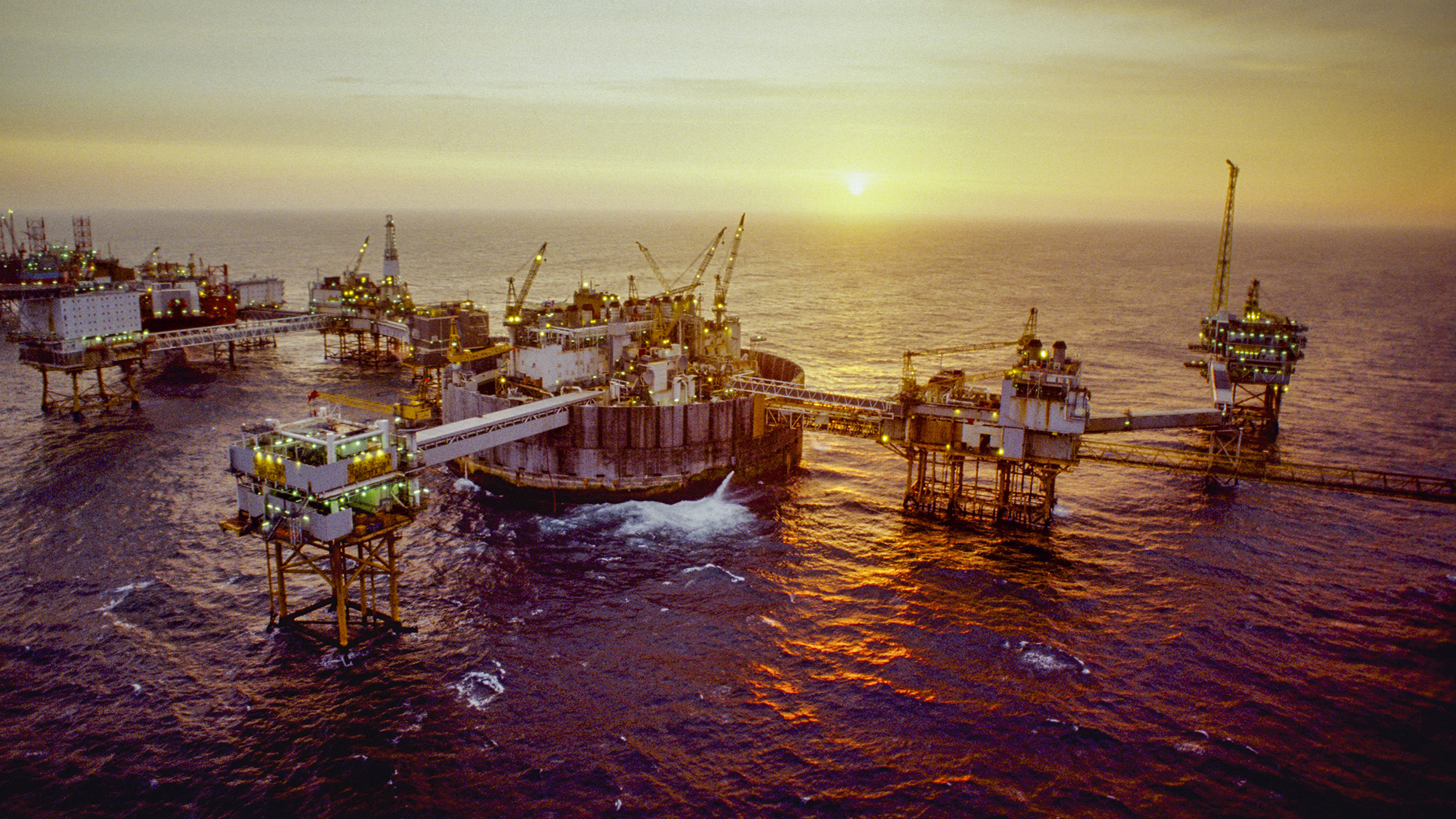 large connected oil rigs in offshore waters with yellow sunrise in the background 